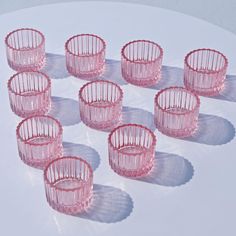 six pink glass cups sitting on top of a white table next to another set of glasses