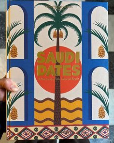 a person holding up a book with an image of a palm tree on the cover