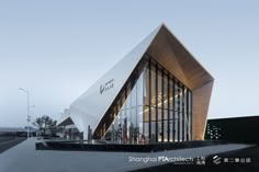 an architecturally designed building on the side of a road at dusk with people walking by