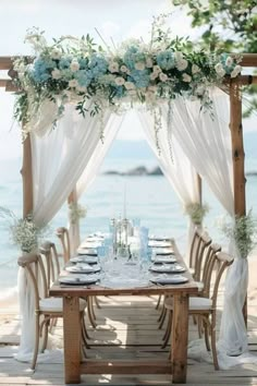 an outdoor table set up with flowers and greenery on the beach for a wedding