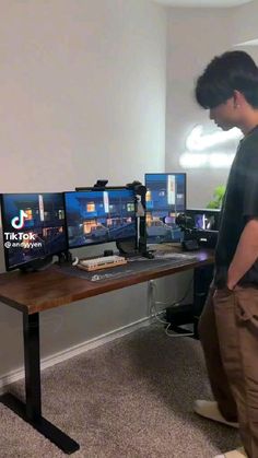 a man standing in front of three computer monitors on top of a wooden desk next to a wall