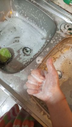 a person washing their hands in a sink with soap on the bottom and water running down the drain