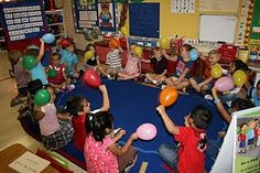 a group of children sitting around each other in a room with balloons on the floor