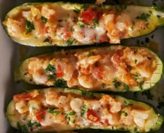 three zucchini boats with shrimp and tomatoes on them in a white dish, ready to be eaten