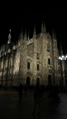 people are standing in front of a large building at night with lights shining on it