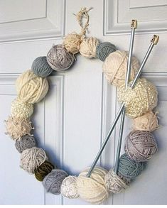 a yarn wreath with knitting needles and balls of yarn hanging on the front door,