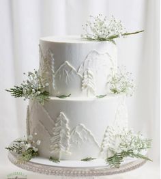 a three tiered cake with white frosting and greenery on top, sitting on a platter