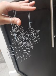 someone is holding some silver ornaments in front of a refrigerator door that has snowflakes hanging from it