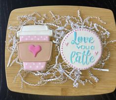 two decorated cookies sitting on top of a cutting board next to each other, with the words love you latte written in frosting