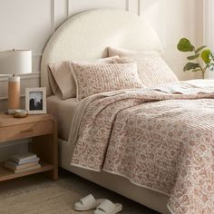 a bed with a white headboard and beige bedspread in a bedroom next to a window