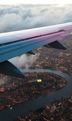 the wing of an airplane flying over a city at night with clouds in the sky