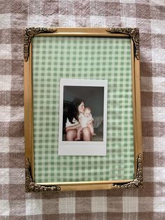 an old photo frame with a baby and a cat in it on a checkered table cloth