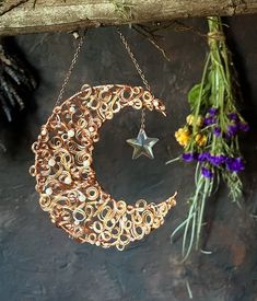 a metal moon and star hanging from a branch with flowers in the background on a slate surface