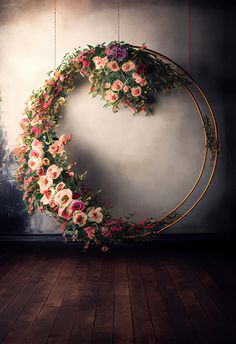 a circular wreath with pink and white flowers hanging from it's sides on a wooden floor