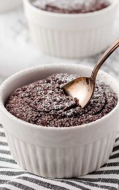 a spoon with some food in it on a table next to another bowl filled with chocolate pudding