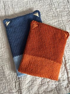 two knitted towels sitting on top of a bed next to each other in orange and blue