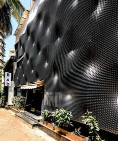 the building is made out of metal mesh and has plants growing in front of it