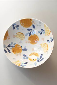 a white bowl with oranges and blue leaves on the rim is sitting on a table