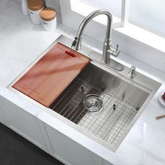 a stainless steel kitchen sink with wooden cutting board