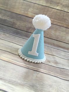 ***Please read shop announcement for current processing times and updates.Your birthday boy will look absolutely adorable in this mini birthday hat for his half birthday or whole birthday!  Perfect for a party or photo shoot. The hat is available in 2 sizes, Mini which is 5 inches tall and 4 inches wide or Full size which is 7 inches tall by 5 inches wide.It features baby blue felt with a white number of your choice. White mini pom pom ribbon is attached along the base of the hat with a yarn Pom Baby Boy First Birthday Party, Diy First Birthday, Blue And White Party, Ideas For First Birthday, Birthday Party Blue, First Birthday Hat, 1st Birthday Hats, First Birthday Hats, 1st Birthday Pictures