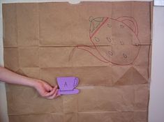 a paper bag with a drawing on it and someone's hand holding a purple cup