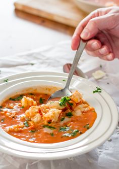 a person is holding a spoon in a bowl of soup with shrimp and parsley