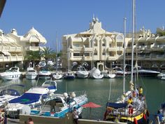 many boats are docked in the water near some buildings and people walking on the sidewalk