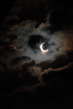 the moon is seen through clouds as it passes in front of a dark cloudy sky