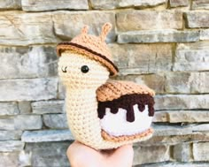 a small crocheted toy is held up in front of a brick wall with a piece of food on it