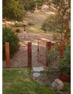 a woman walking down a path through a lush green field next to a metal gate