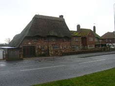 an old brick building with thatched roof next to a street in the country side