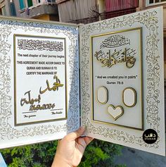 an open book with arabic writing on the pages and two pictures in gold frames, held up by someone's hand