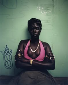 a woman in a pink tank top and black skirt sitting against a wall with her arms crossed