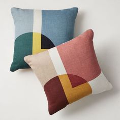 two pillows with different colors on them sitting next to each other in front of a white wall