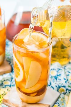 a pitcher pouring lemonade into a glass filled with ice cubes and sliced orange slices