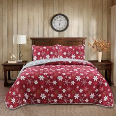 a red and white comforter set with snowflakes on it in front of a clock