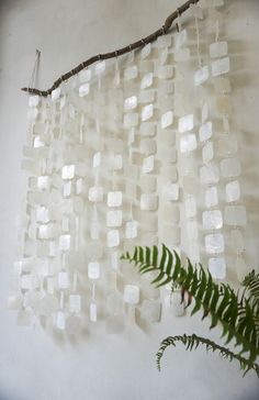 a wall hanging made out of ice cubes on a branch with a fern in the foreground