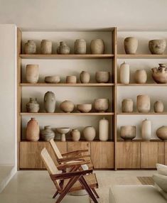 a room filled with lots of vases on shelves next to a chair and table