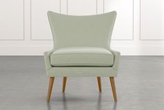 a light green chair with wooden legs in front of a white wall and gray floor