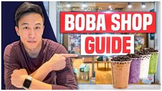 a man pointing at the camera in front of an advertisement for boba shop guide