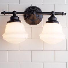 two light fixtures mounted on a white tile wall in a bathroom with dark metal fittings