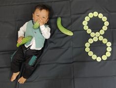 a baby is laying on the ground with cucumbers in front of him and his name spelled out