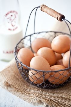 a wire basket filled with brown eggs on top of a table next to a bottle of milk