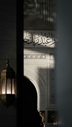 the light shines on an arch and lantern in front of a wall with arabic writing