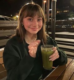 a woman holding a green smoothie in her right hand and smiling at the camera