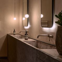 two sinks and mirrors in a bathroom with lights on the wall above them at night