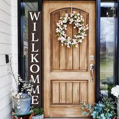 a front door with a welcome sign and wreath on the side walk next to potted plants