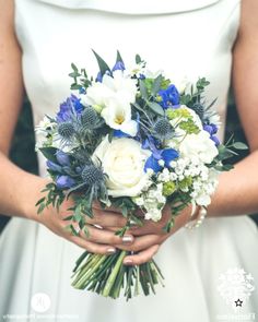 a bride holding a bouquet of white and blue flowers with greenery in her hands