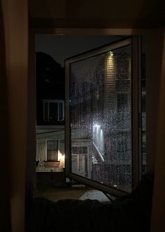 an open window at night with rain falling on the glass and lights shining in the distance