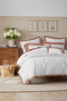 a bed with white and brown comforters in a bedroom next to a basket full of flowers